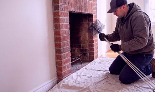 Mason kneeling at a brick hearth, tending the flue by hand